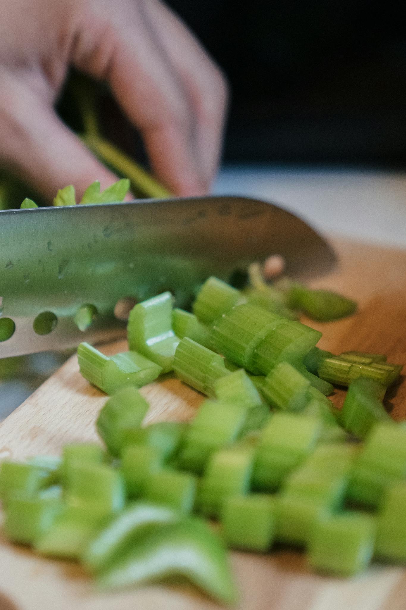 Close-up of celery being sliced on a wooden board, showcasing food preparation.